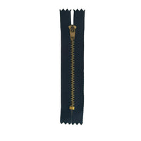 A single black  zipper with a gold-toned metal pull and teeth, laid flat on a white sheet of paper.