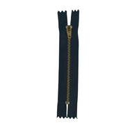 A single black zipper with a gold-toned pull tab, laid vertically on a textured white paper background.