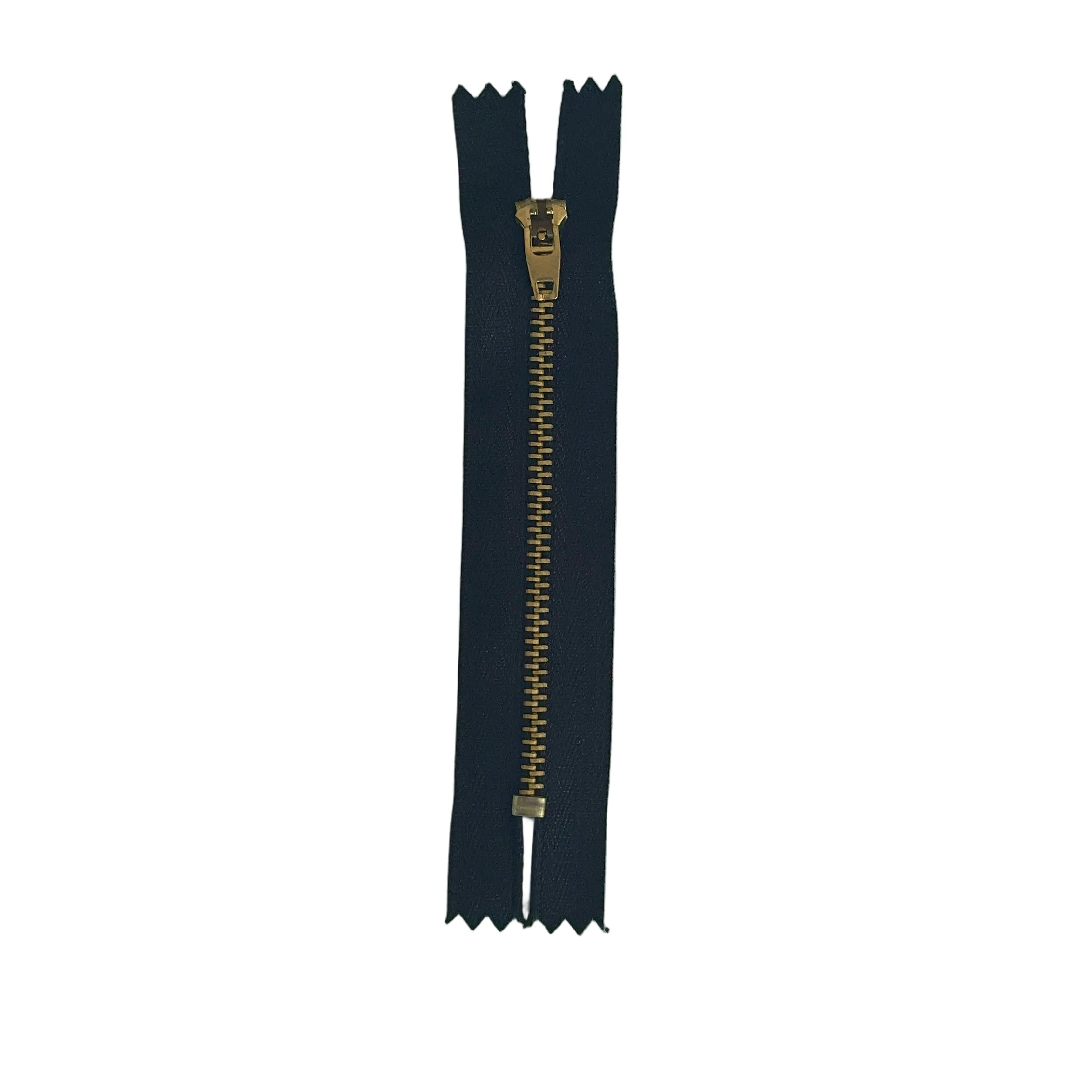 A single black zipper with a gold-toned pull tab, laid vertically on a textured white paper background.