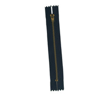 A single black zipper with a gold pull tab and gold teeth, placed vertically on a white textured paper background.