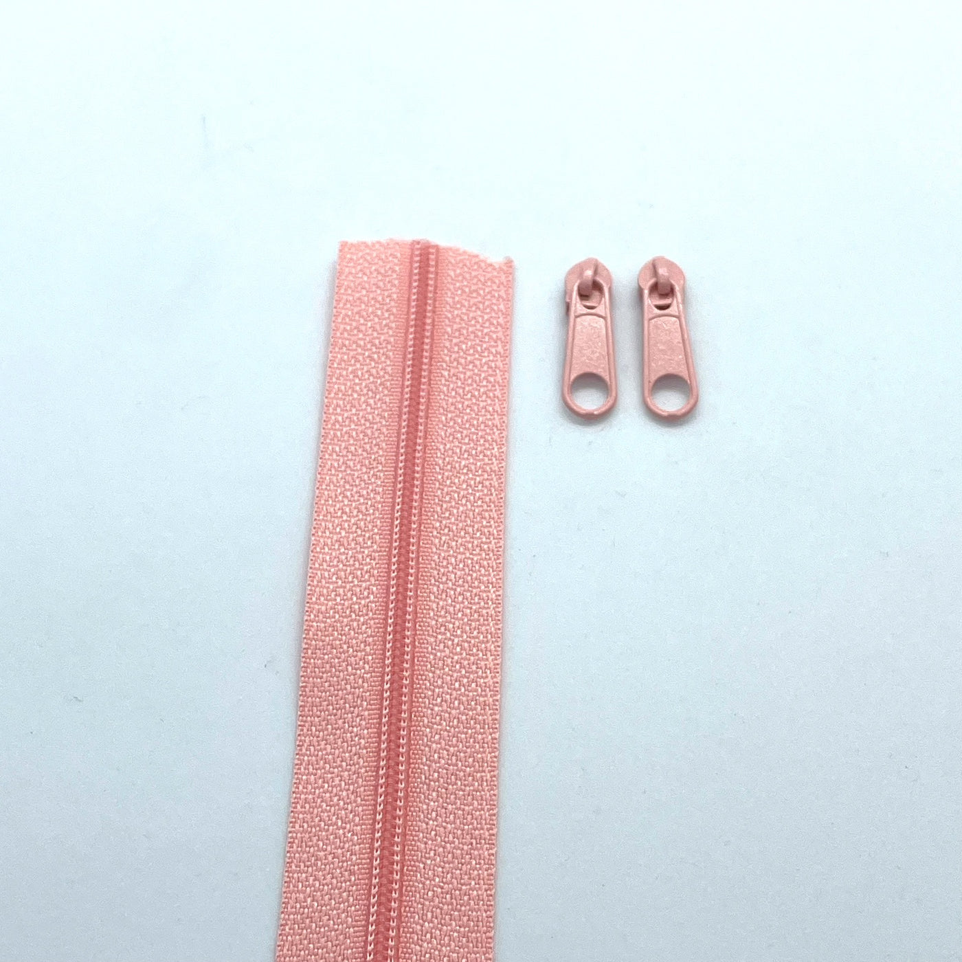 Photo of coral continuous zipper rolls in size 3, available in various colors. Matching sliders/zipper heads included at 2 per meter. Size 3 refers to the size of the coils when closed at 3mm