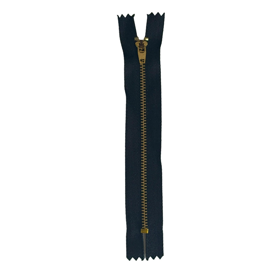 A single black zipper with a gold-toned metal pull tab, placed vertically on a textured off-white paper background.