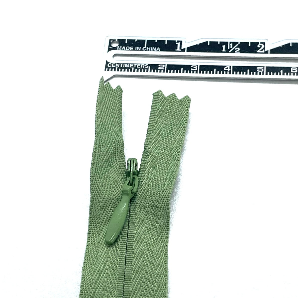 Photo of dusky sage green invisible or concealed zips available in many different colours and sizes. Great for achieving a professional finish in your products. Invisible zippers are perfect for dressmaking, cushions, crafts, etc., where you don't want your zipper showing. Installing them can be tricky without the right foot on your machine; a normal zipper foot is for installing standard zippers, while you will need an invisible zipper foot for a professional result