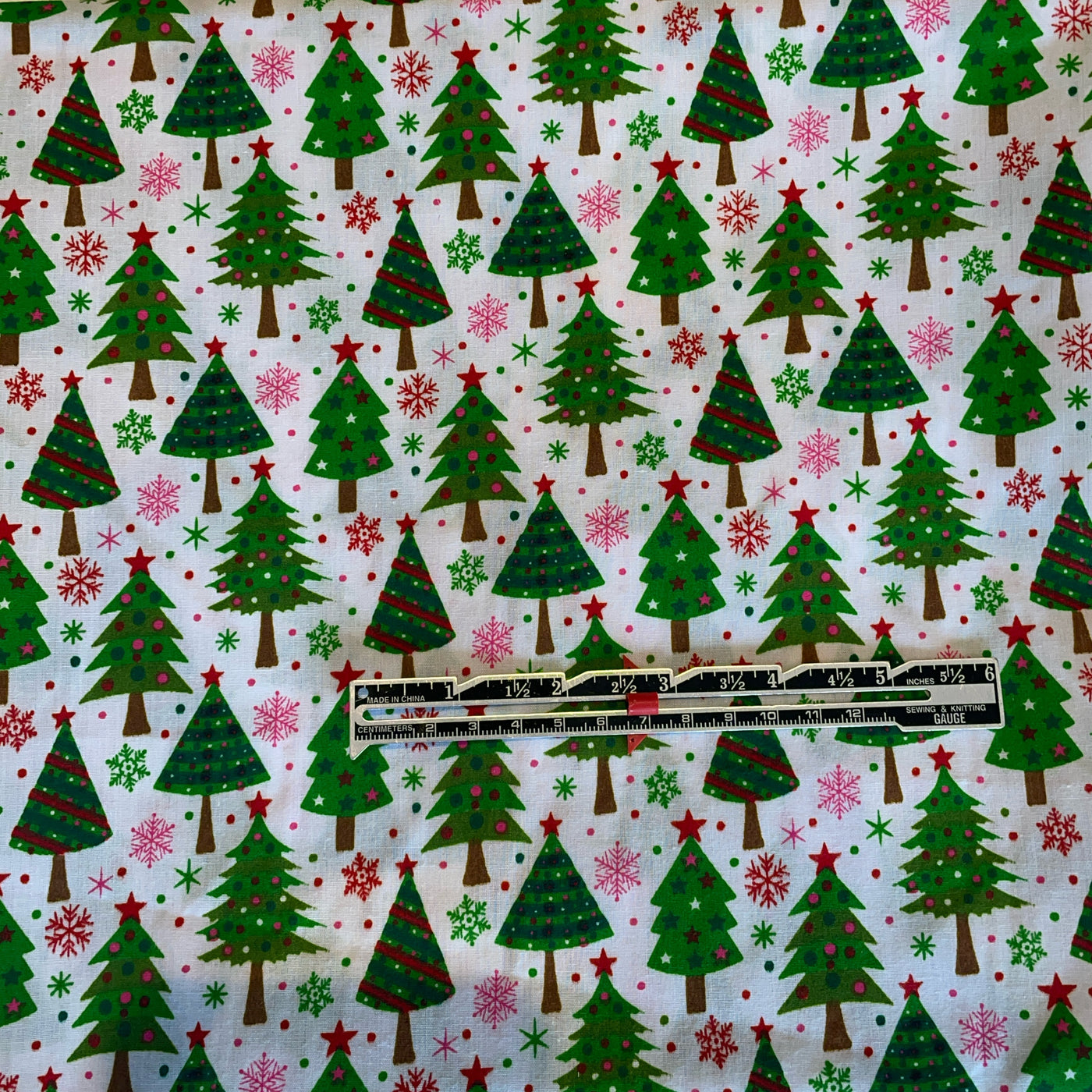 Fabric with Christmas tree pattern featuring green trees, red stars, and pink snowflakes on a white background.