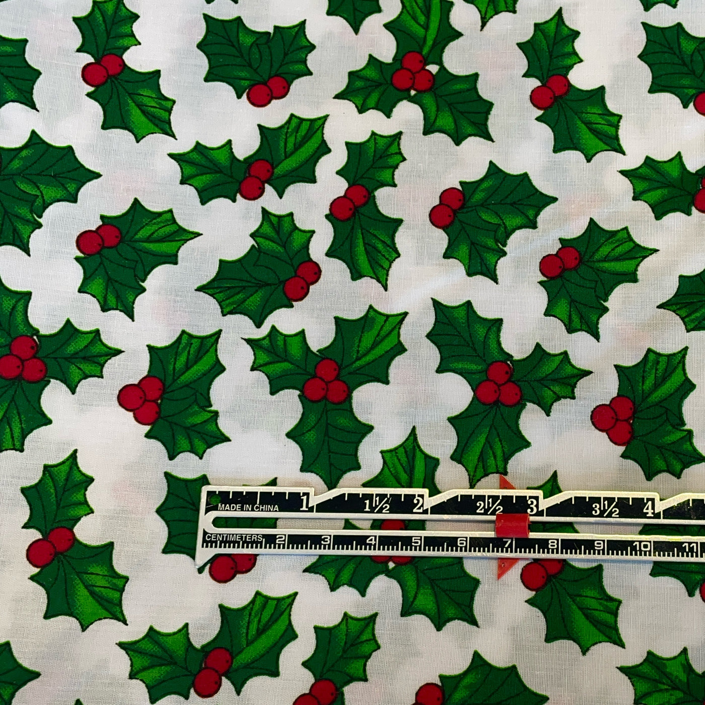 Pattern of green holly leaves and red berries on a white background with a ruler at the bottom.