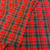A close-up of red tartan plaid fabric with fringe edges, featuring intersecting black, green, and yellow stripes.