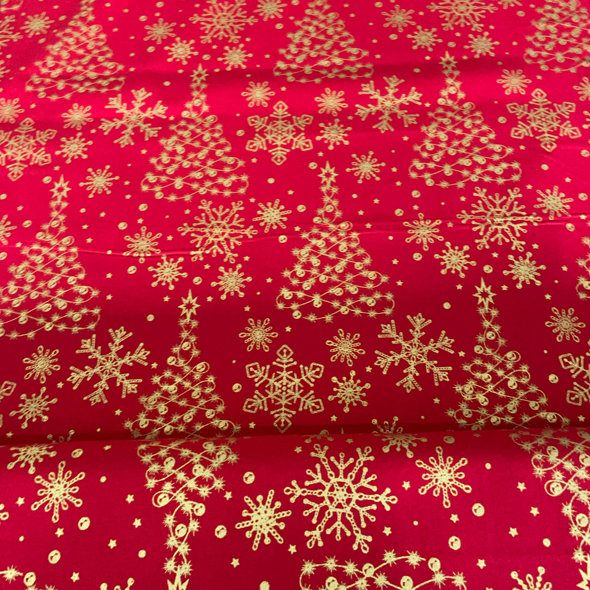 Bright red fabric with a repeating gold holiday print featuring Christmas trees, snowflakes, stars, and small decorative motifs.