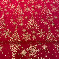 Red fabric with a repeating gold pattern of Christmas trees, snowflakes, and stars, shown folded to reveal the texture and underside.