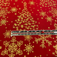 Red fabric with a gold glitter Christmas tree and snowflake pattern, shown with a measuring tape to indicate scale.