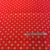Red fabric with a repeating gold geometric star pattern, shown flat with a small white measurement tape measure placed near the bottom center.