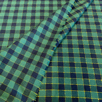 A close-up of plaid fabric with a green and navy blue checkered pattern outlined by thin yellow stitching, folded diagonally across the frame.