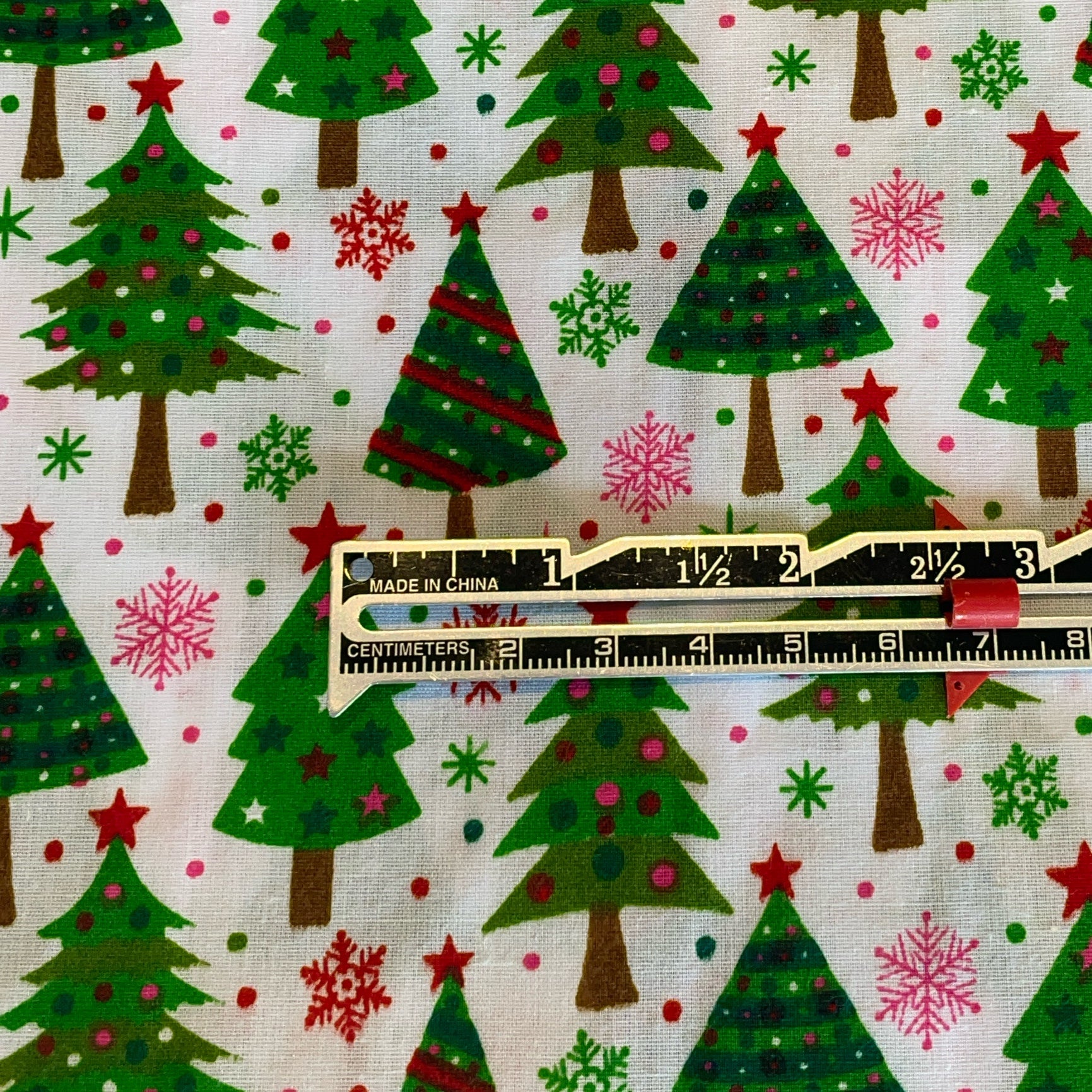 Christmas-themed fabric with trees, snowflakes, and stars, featuring a ruler for scale.