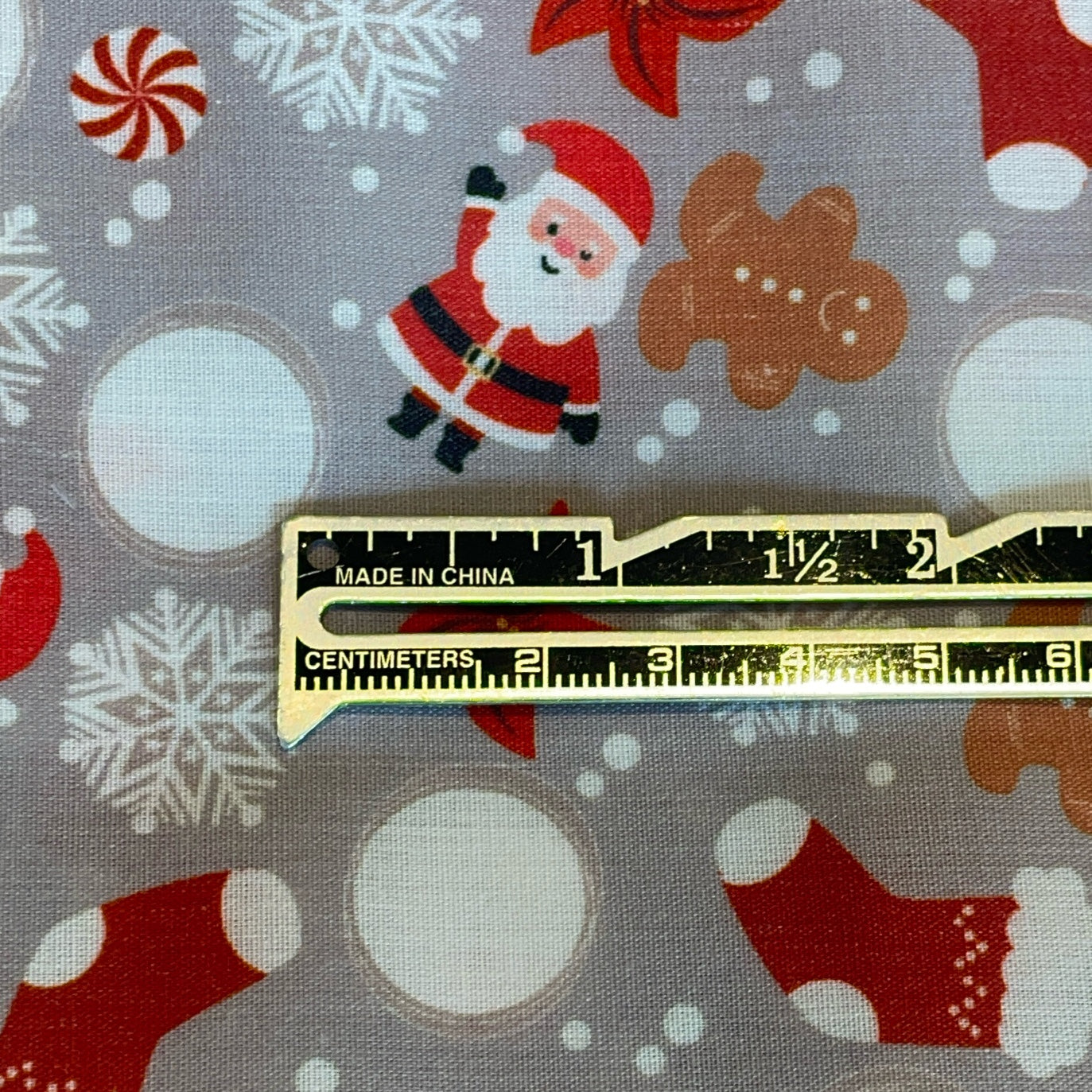 Gold ruler on fabric with Christmas patterns including Santa Claus, gingerbread men, and snowflakes.