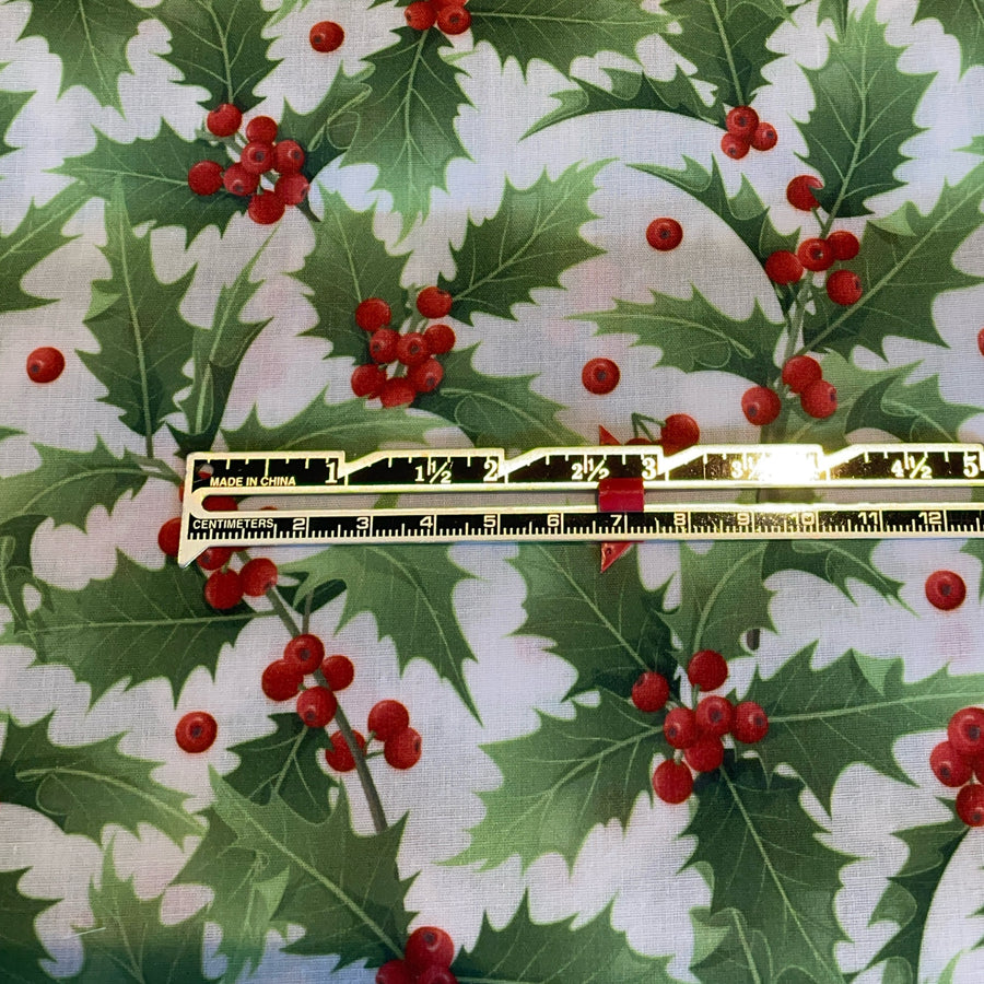 Fabric with holly leaves and berries pattern and a ruler for scale.