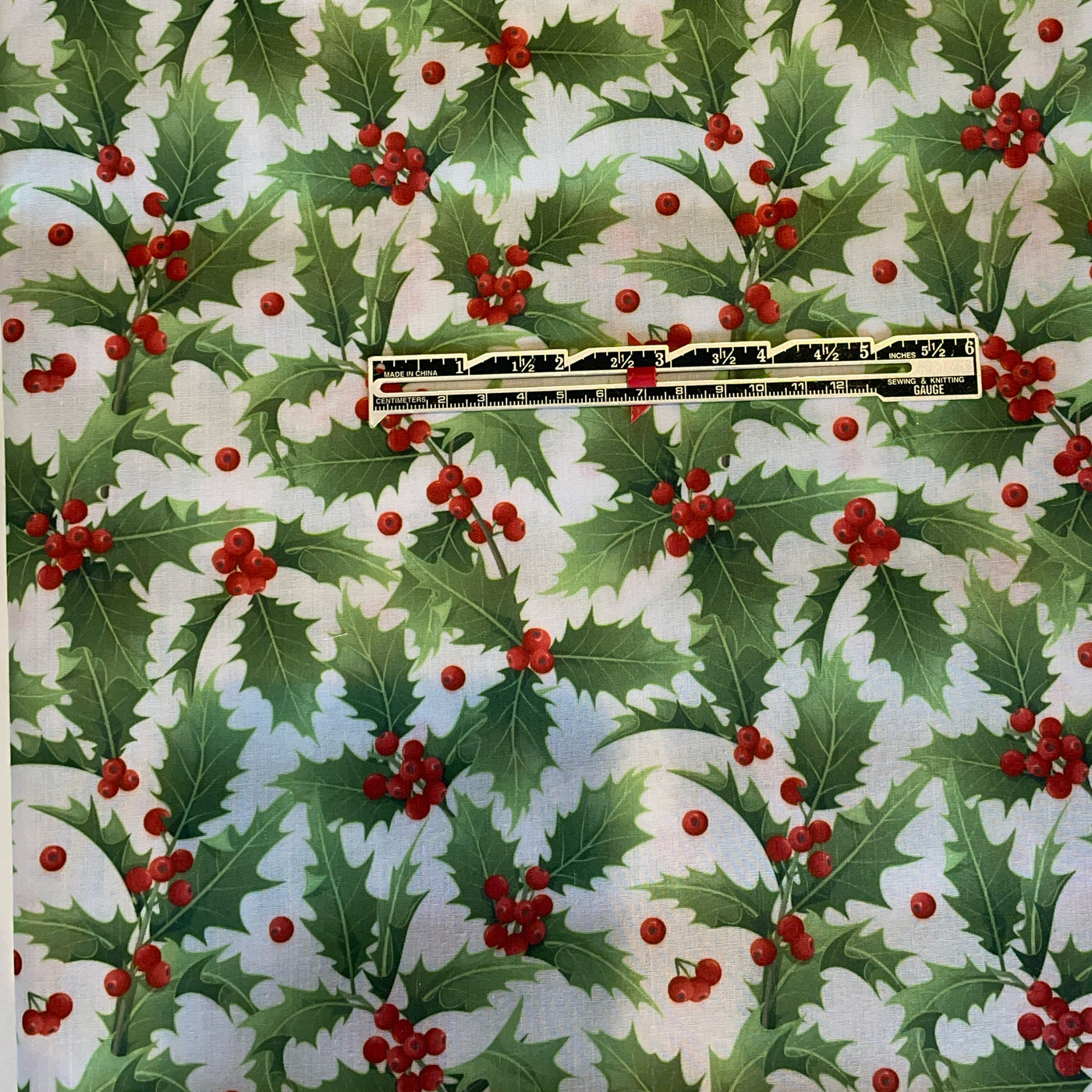 Holly leaf and berry pattern with a ruler for scale on a white background