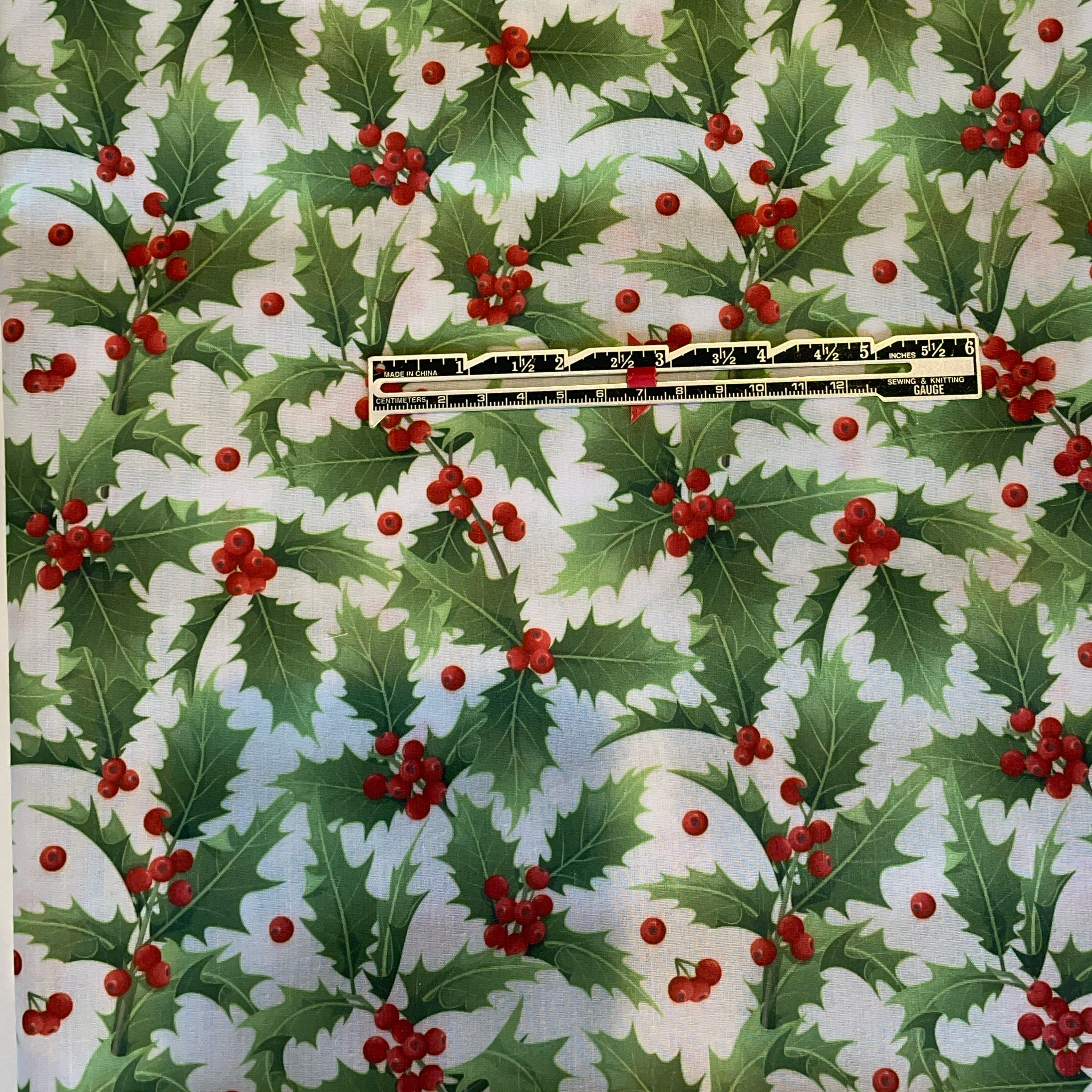Holly leaf and berry pattern with a ruler for scale on a white background