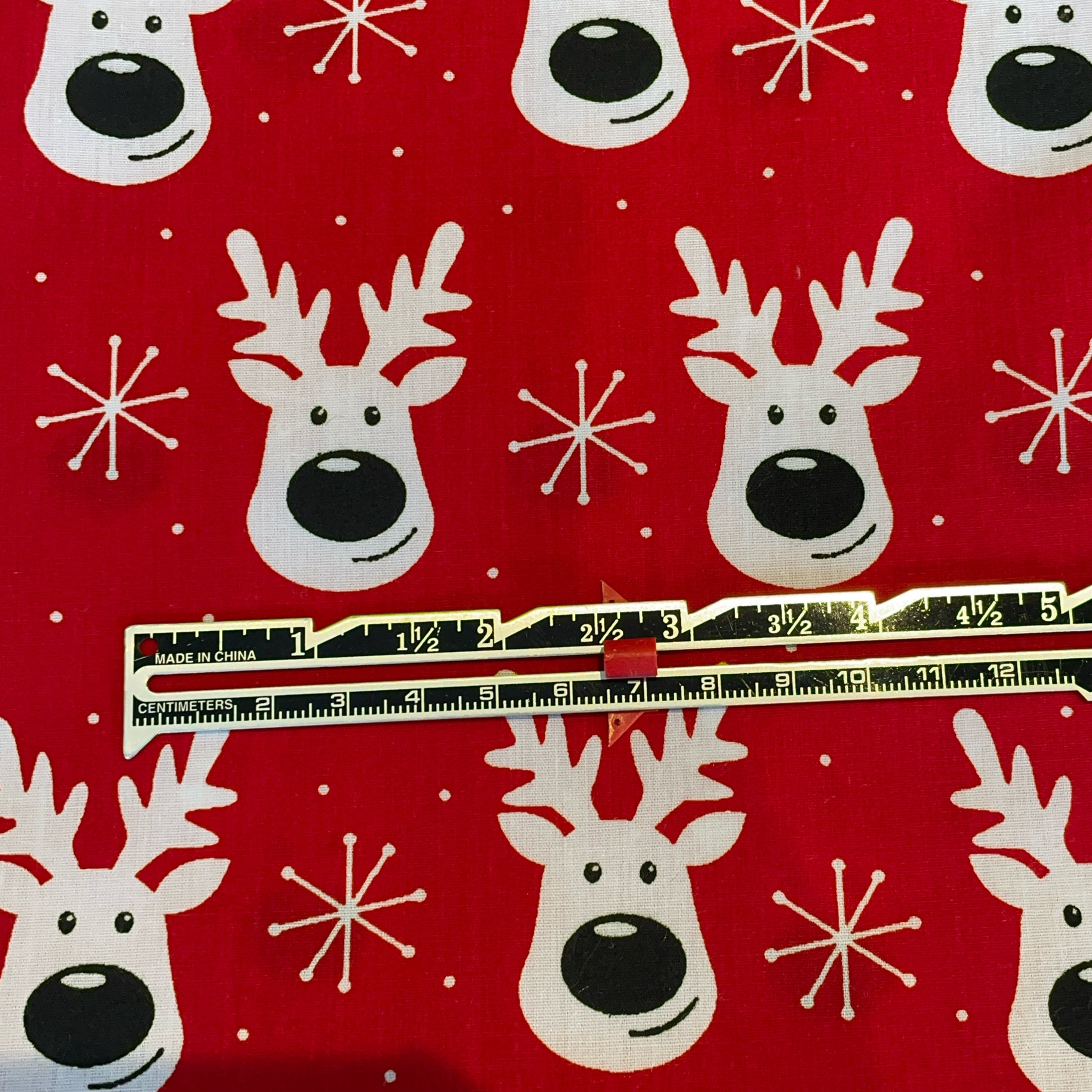 Red fabric with white reindeer and snowflake patterns, ruler for scale