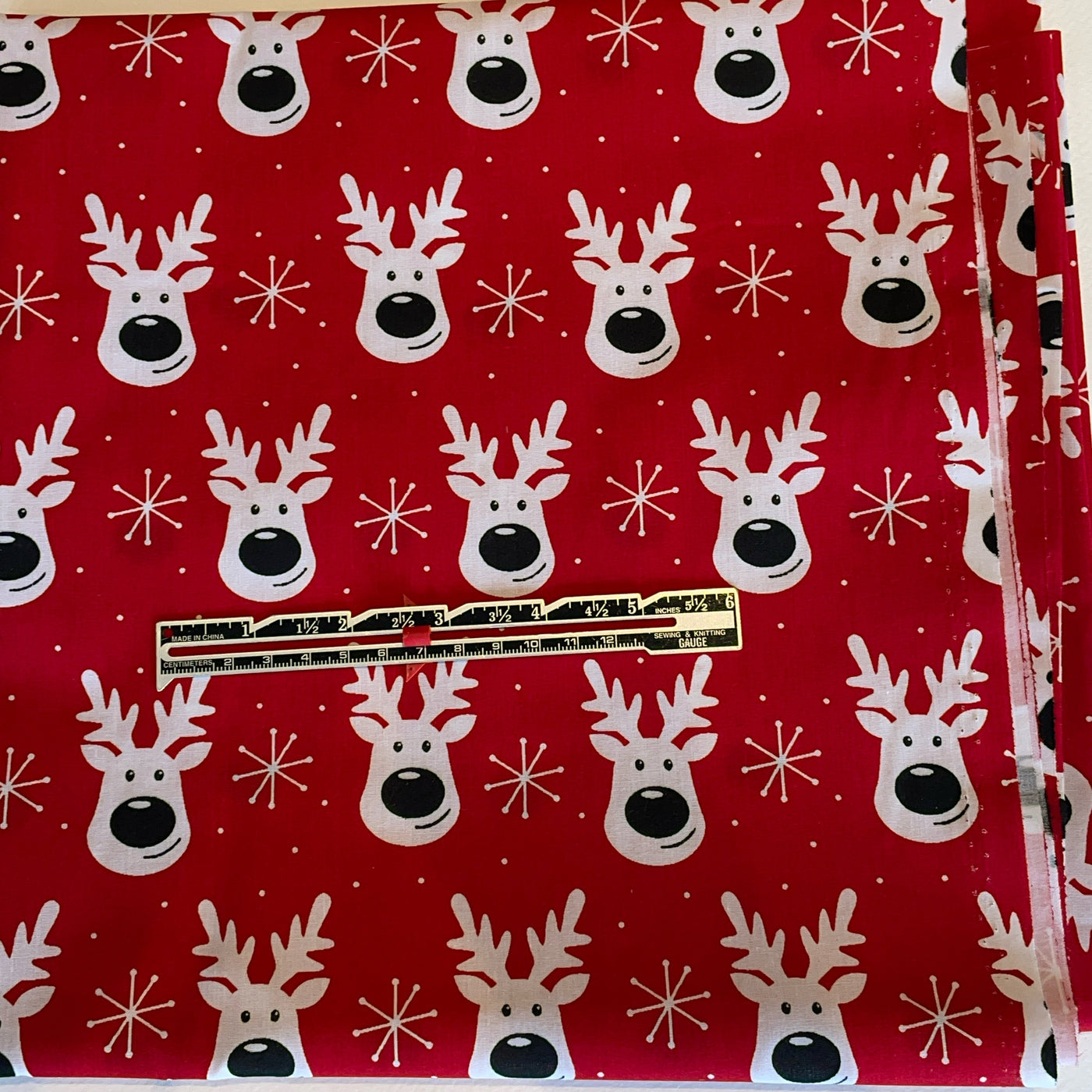 Red fabric with white reindeer and snowflake pattern, gold zipper visible