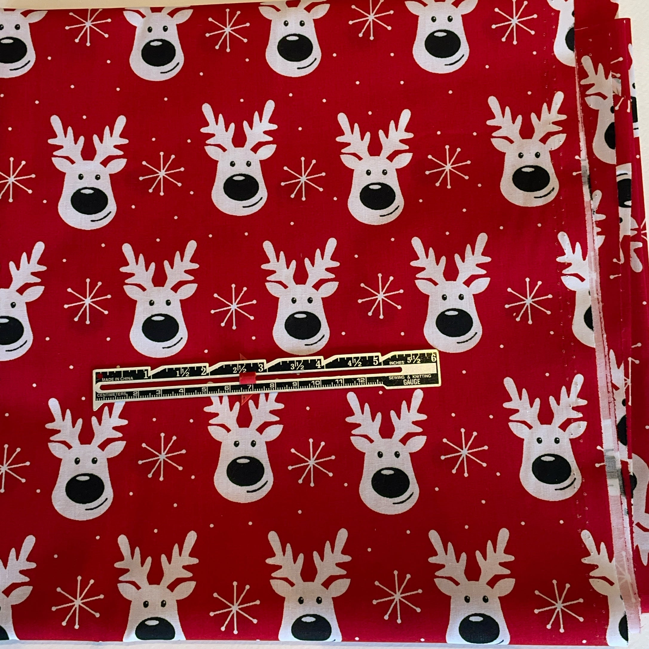 Red fabric with white reindeer and snowflake pattern, gold zipper visible