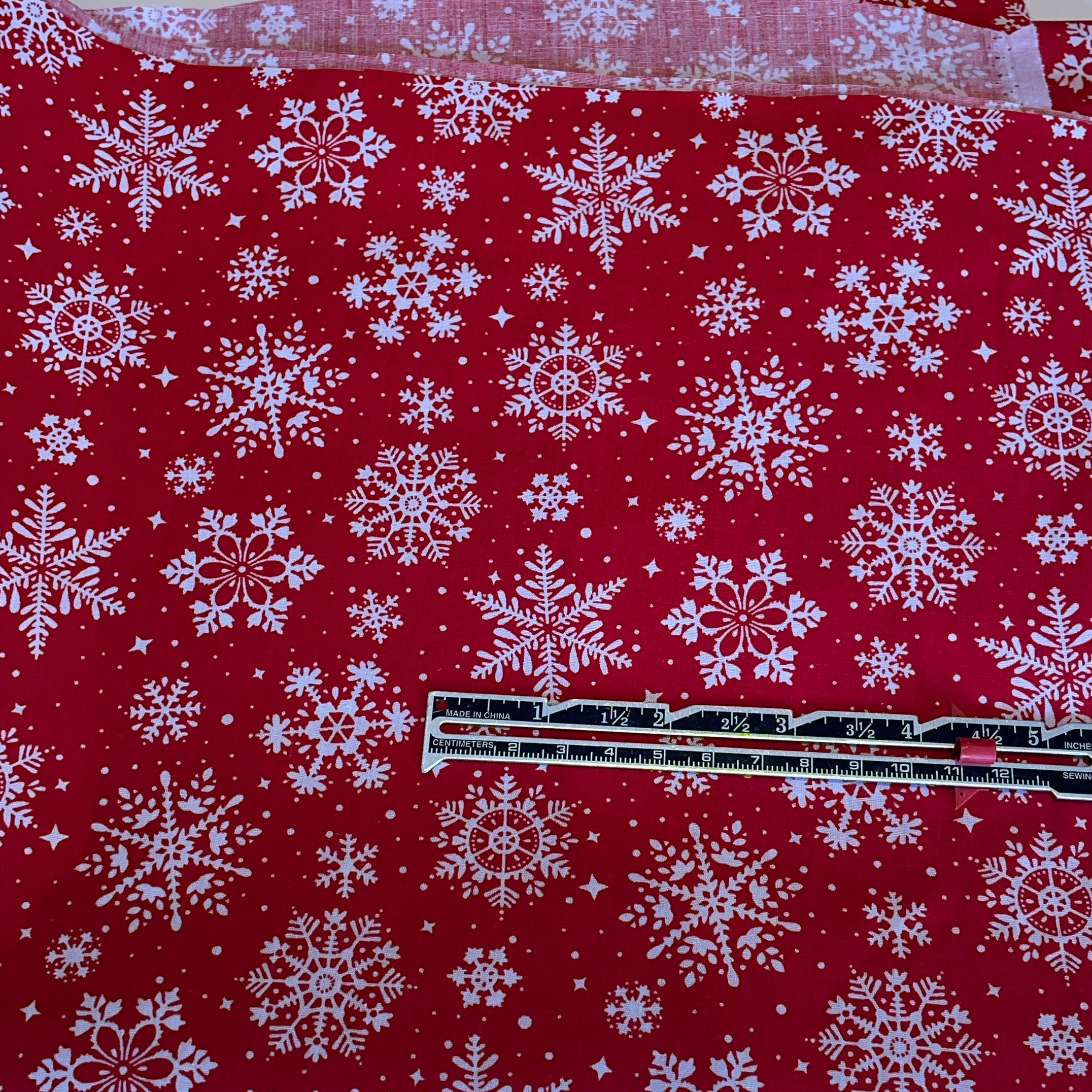 Red fabric with white snowflake pattern and a ruler for scale.